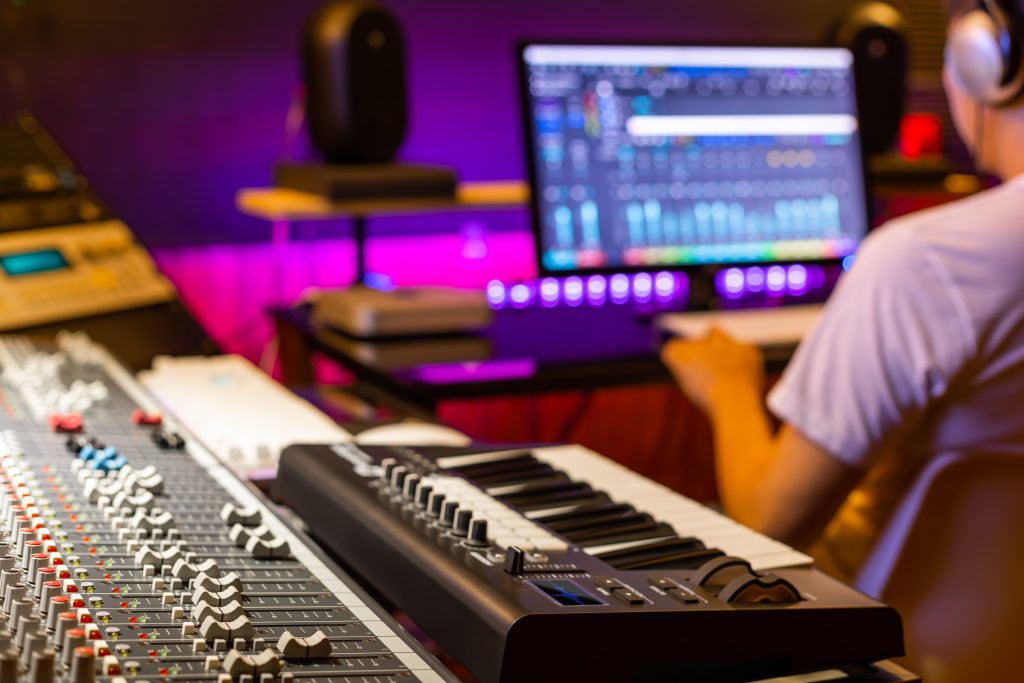 back of male asian professional producer working in recording studio, focus on mixing console fader. music production concept